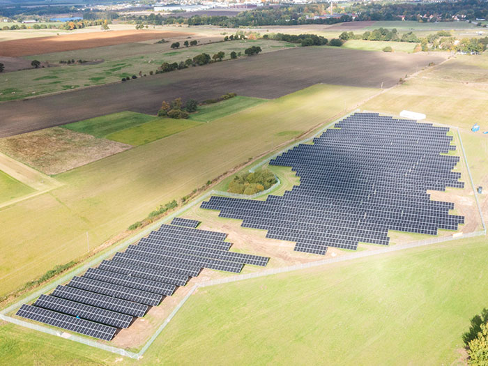 Drönarvy över tusentals solpaneler på jordbruksmark.