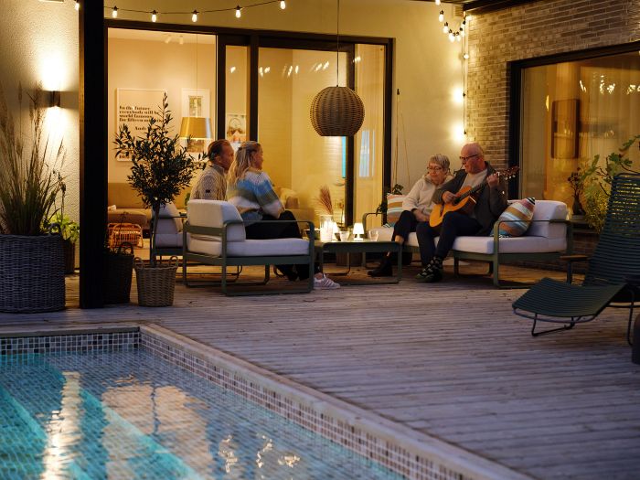 familj som sitter utomhus på kvällen intill en villa med pool